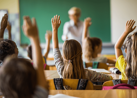iStock-1000887536_Back view of elementary students raising their arms on a class.jpg